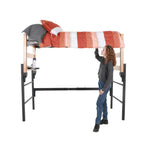 A wooden and metal loft with a pop-out shelf and orange and white comforter being made by an actor