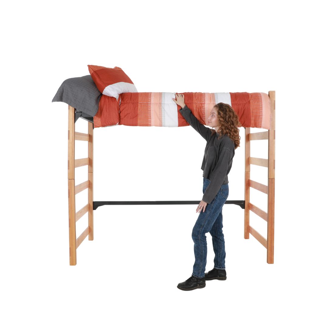 A wooden bed loft with an orange and white comforter being made by an actor