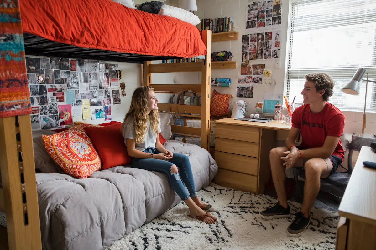 Two college students smiling in a dorm room with an orange and grey color palette